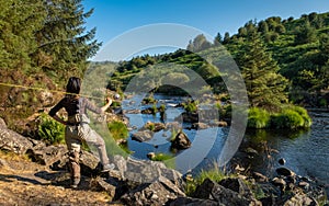 An asian female fly fisher women wearing waders, resting a rod on her shoulder