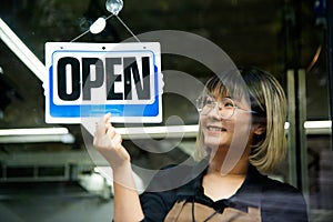 Asian female hairdesser of salon shop turning round open sign on a door.