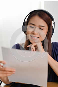 Asian female with headphones listening her tutor teaching online and reading a paper