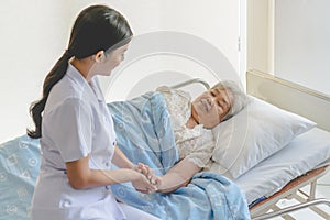 Asian female home nursing holding hand of older lady on the bed and encouraging patient