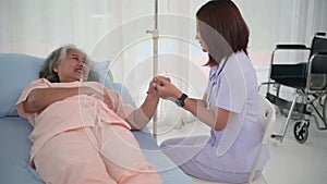 Asian female home nursing holding hand of older lady on the bed and encouraging patient