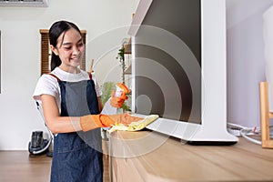 Asian female housekeeper cleaning the house using spray and cleaning cloth at the table in the living room