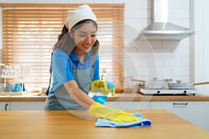 Asian female housewife using table cloth and sprayer in kitchen at home