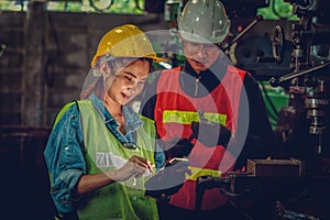 Asian female industrial worker make data input to manufacturing io device with supervision of factory chief engineer