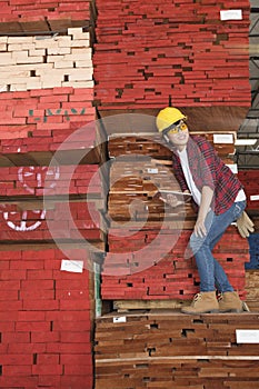 Asian female industrial worker standing on stacked wooden planks holding tablet PC