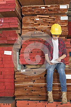 Asian female industrial worker using tablet PC while sitting on stacked wooden planks