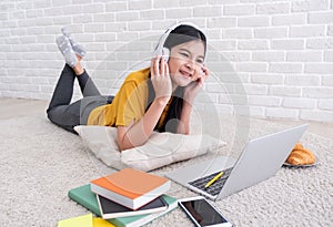 Asian female listen to music and use laptop computer to work at home.woman lay down on carpet at brick wall.working online