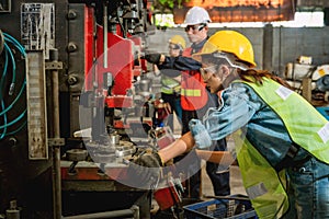 Asian female and male manufacturing workers operating steel drilling machine together in line of metal work production factory