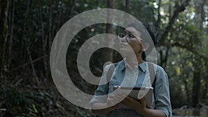 Asian female nature conservationist looking around while working in the rainforest with digital tablet in early morning.