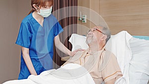 Asian female nurse wear face mask care and check on senior male smile patient on hospital bed in hospital private room