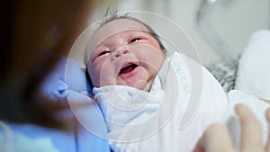 Asian female parent holding newborn baby with care on bed at hospital. woman looking at infant.