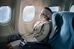 Asian female passenger in business class wearing face mask during the COVID pandemic sitting on airplane to prevent coronavirus in