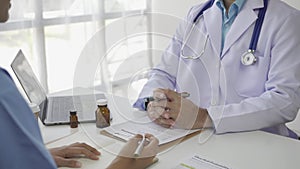 Asian female patient sitting at a table listening to a medical professional with a stethoscope explaining