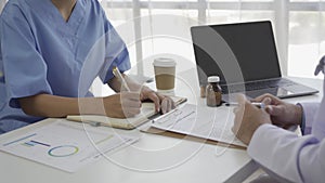 Asian female patient sitting at a table listening to a medical professional with a stethoscope explaining