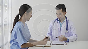 Asian female patient sitting at a table listening to a medical professional with a stethoscope explaining