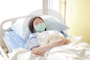 Asian female patients Wear a blue mask and lie in a hospital bed.