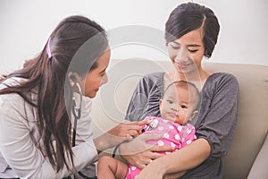 Asian female pediatrician examining a baby girl in the mother la