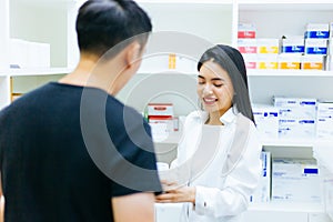 Asian female pharmacist doctor in professional gown explaining and giving advice with male client in drugstore shop.