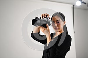 Asian female photographer with professional camera working in modern photo studio