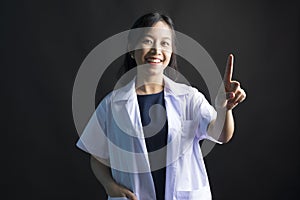 Asian female physician, Med student or resident doctors standing and pointing finger on black background.