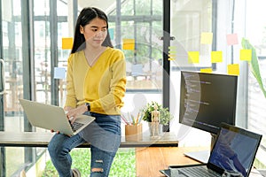 Asian female programmer for yellow shirt sit on the shelf and place laptop on leg.She stared at computer screen on the table and