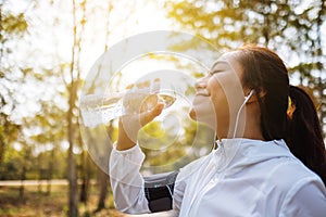 An asian female runner drinking water from bottle after jogging in city park