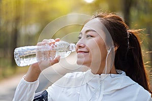 An asian female runner drinking water from bottle after jogging in city park
