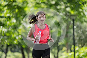 Asian female runner running on the street and holding water bottle in the park