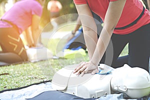 Asian female or runner woman training CPR demonstrating class in park by put hands and interlock finger over CPR doll give chest