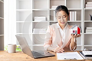 Asian female saleswoman holding key to customer and recommending interest rates on home delivery