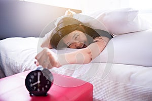 Asian female stretching her hand to ringing alarm to turn off alarm clock,Woman hates getting stressed waking up early