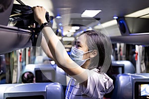 Asian female student stowed her backpack in a overhead storage on the school bus,child girl wearing protective mask to safety from photo