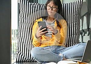 Asian female students wearing glasses listening to music from smartphones and headphones