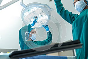 Asian female surgeon and colleague adjusting lights in operating theatre for operation