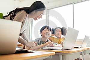 Asian Female teacher helping pupils using laptop