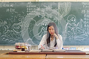 Asian female teacher sitting in a classroom marking homework of the students