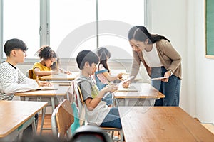 Asian Female Teacher talking Pupils studying at desks