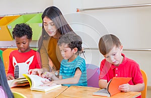 Asian female teacher teaching diversity kids reading book in classroom,Kindergarten pre school concept. photo
