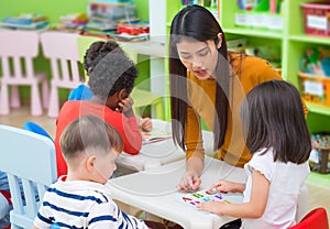 Asian female teacher teaching mixed race kids reading book in cl