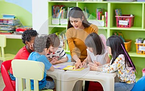 Asian female teacher teaching mixed race kids reading book in cl