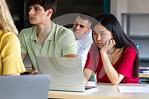 Asian female teen college student in class listening to lecture using laptop to take notes.