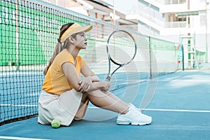 asian female tennis player sitting holding racket on tennis court