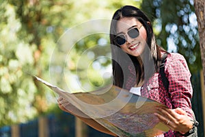 Asian female tourist, wearing sunglasses, holding a map, smilingly looking at the camera photo