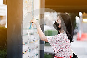 Asian female tourists and face masks looking at city map signs, New Normal Life style, Covid-19 crisis