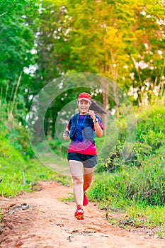 Asian female trail runners, wearing runners, sportswear, practice running on a dirt path in a forest. With a happy mood, there