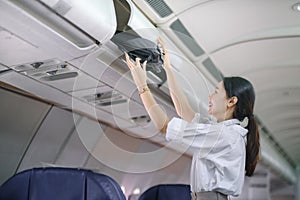 Asian female traveler putting luggage into overhead locker on airplane during boarding.