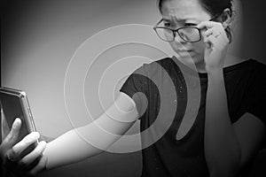 Asian female trying to read something in her mobile phone. poor sight, farsightedness, myopia. Black and white tone