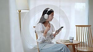 Asian female is unwinding at cafe, selecting songs on smartphone and listening
