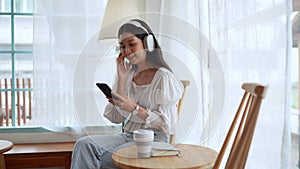 Asian female is unwinding at cafe, selecting songs on smartphone and listening