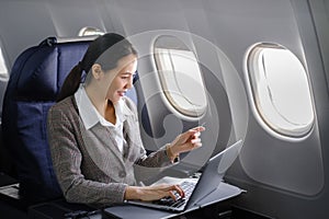 Asian female using laptop computer and holding credit card in airplane, Business traveling and technology concept.